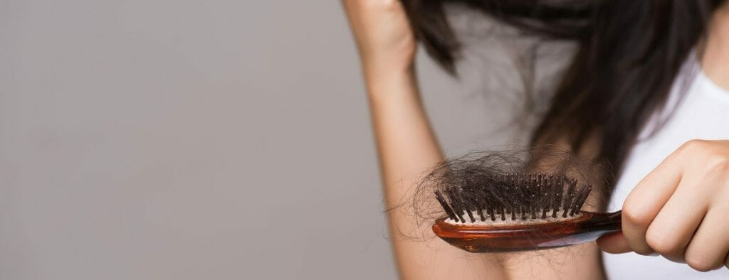 Woman with dark hair holding brush with lots of hair