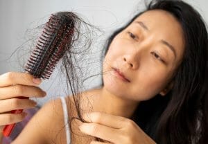 Woman with dark hair looking at brush with tons of hair loss