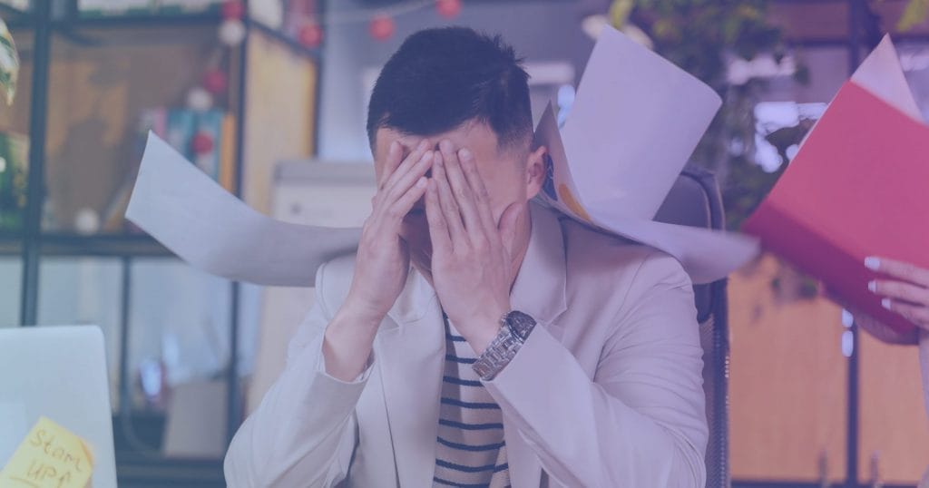 Man at work holding his head while papers swirl around him