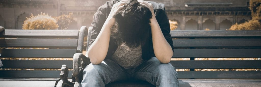 Man sitting on bench holding head in his hands