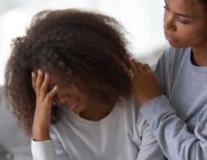 Teenage girl holding head while mom comforts her