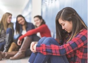 Teenage girl sitting alone and feeling left out near a group of friends