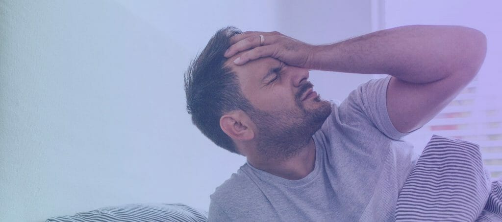 Man laying in bed holding his head in pain