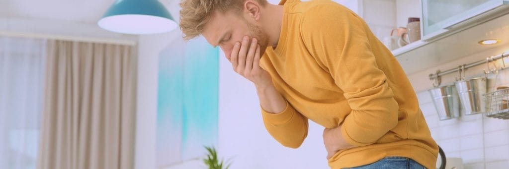 Man with yellow shirt holding stomach and mouth appearing ill