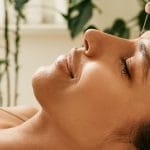 Woman lying down getting acupuncture needles placed in her forehead