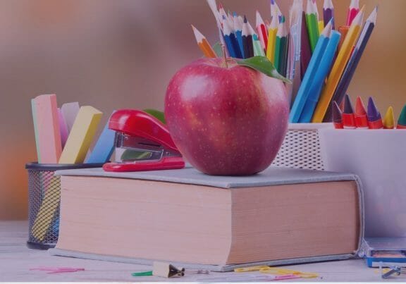 A red apple sitting on a book, colored pencils and school supplies