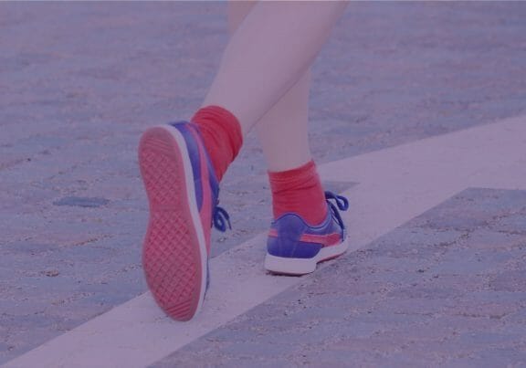 Woman with red socks and blue sneakers walking on a white arrow painted on the street