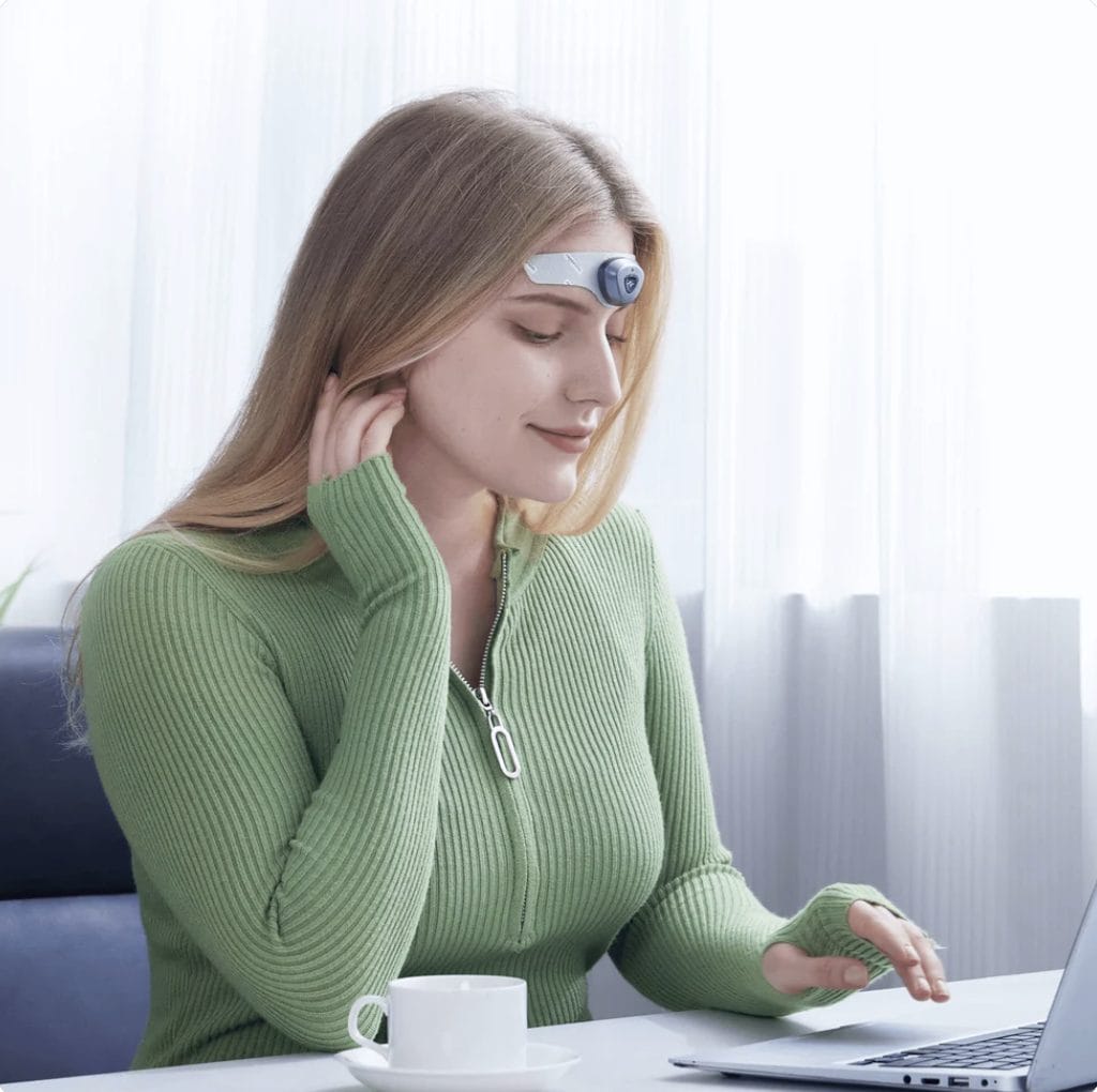 Woman sitting at desk wearing headaterm device on her forehead