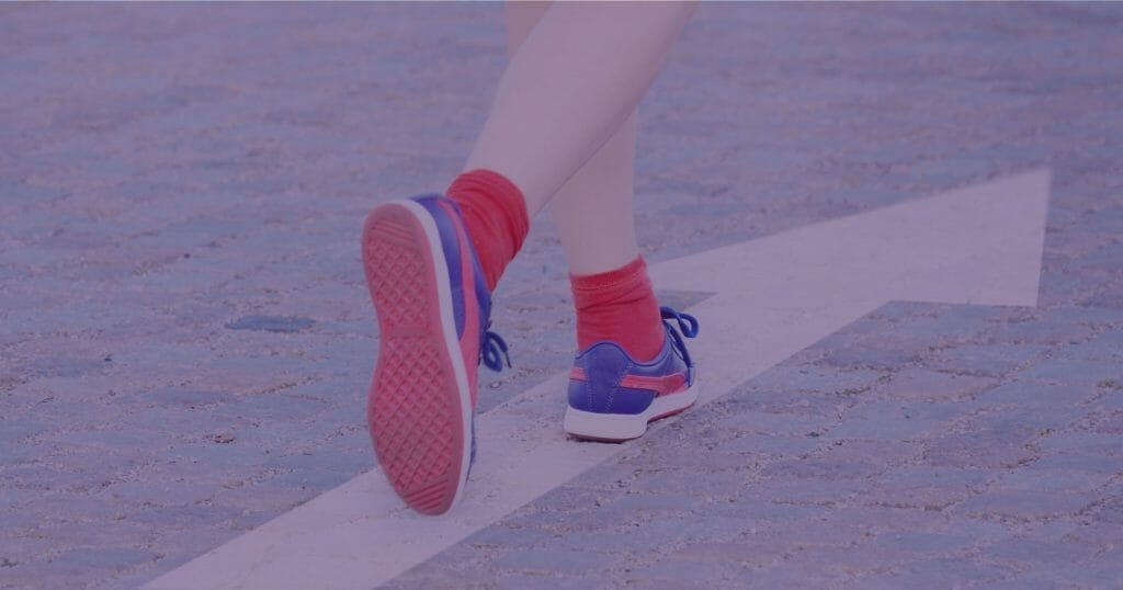 Woman with red socks and blue sneakers walking on a white arrow painted on the street