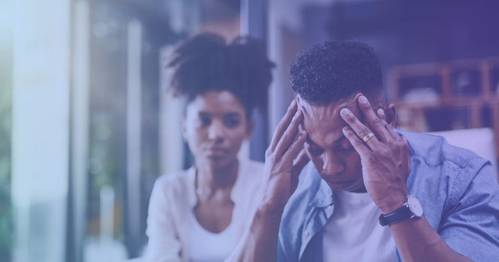 Man and woman sitting on couch, man holding his head